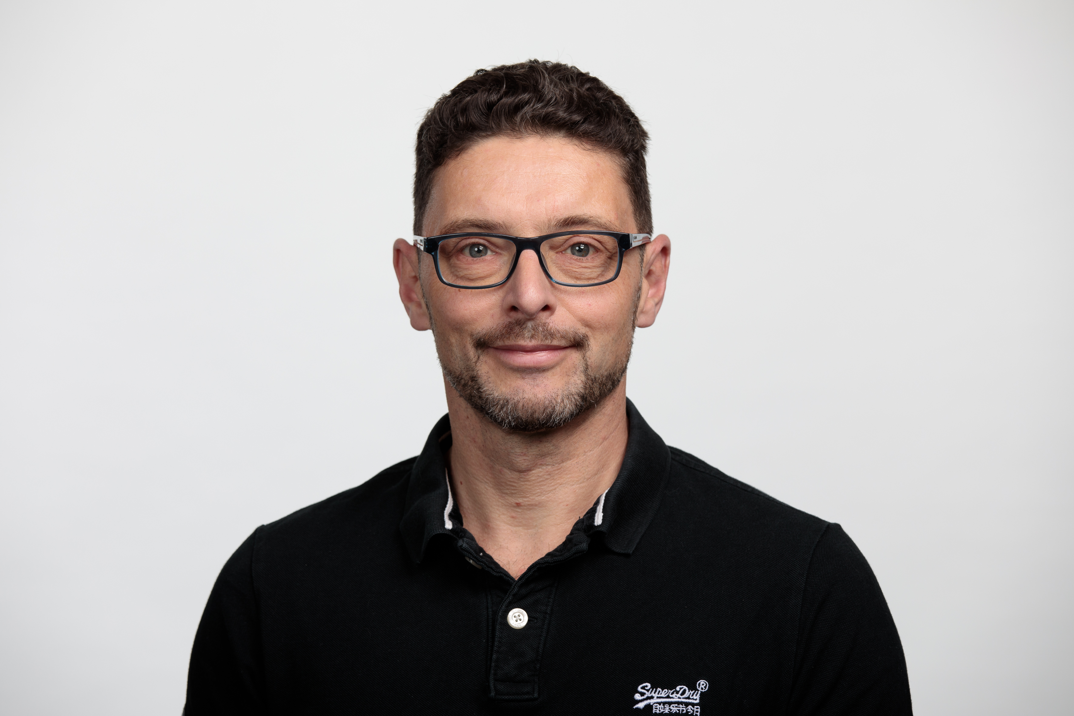 Portraifoto eines weissen Mannes mit kurzen schwarzen Haaren und Brille