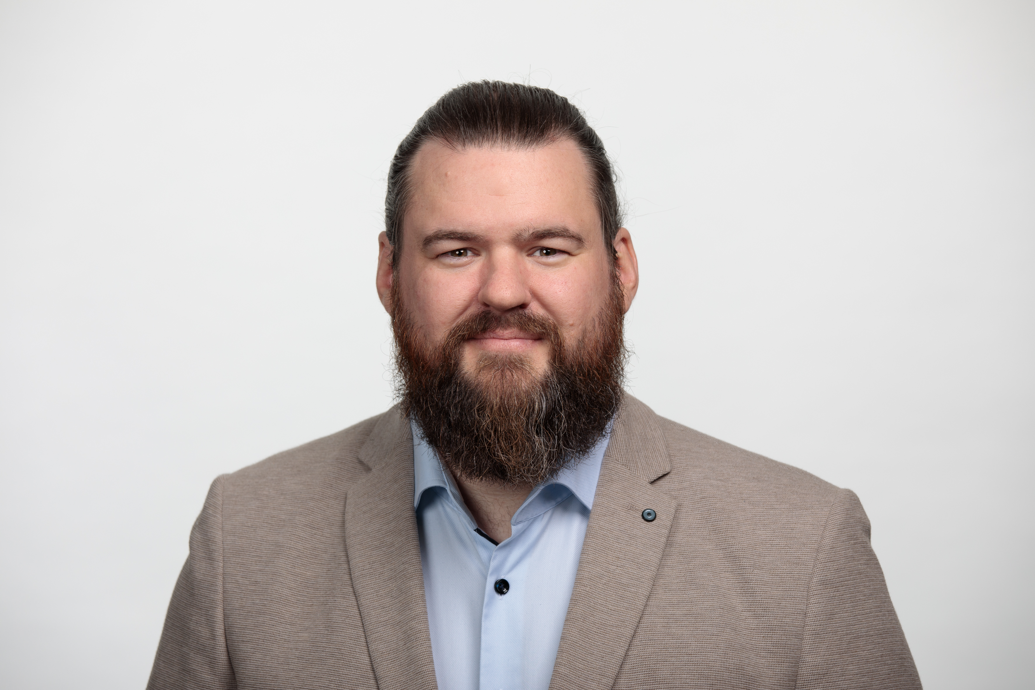 Portraitbild eines weissen Mannes mit braunen langen Haaren und Vollbart, er traegt ein helles Hemd und Jacket