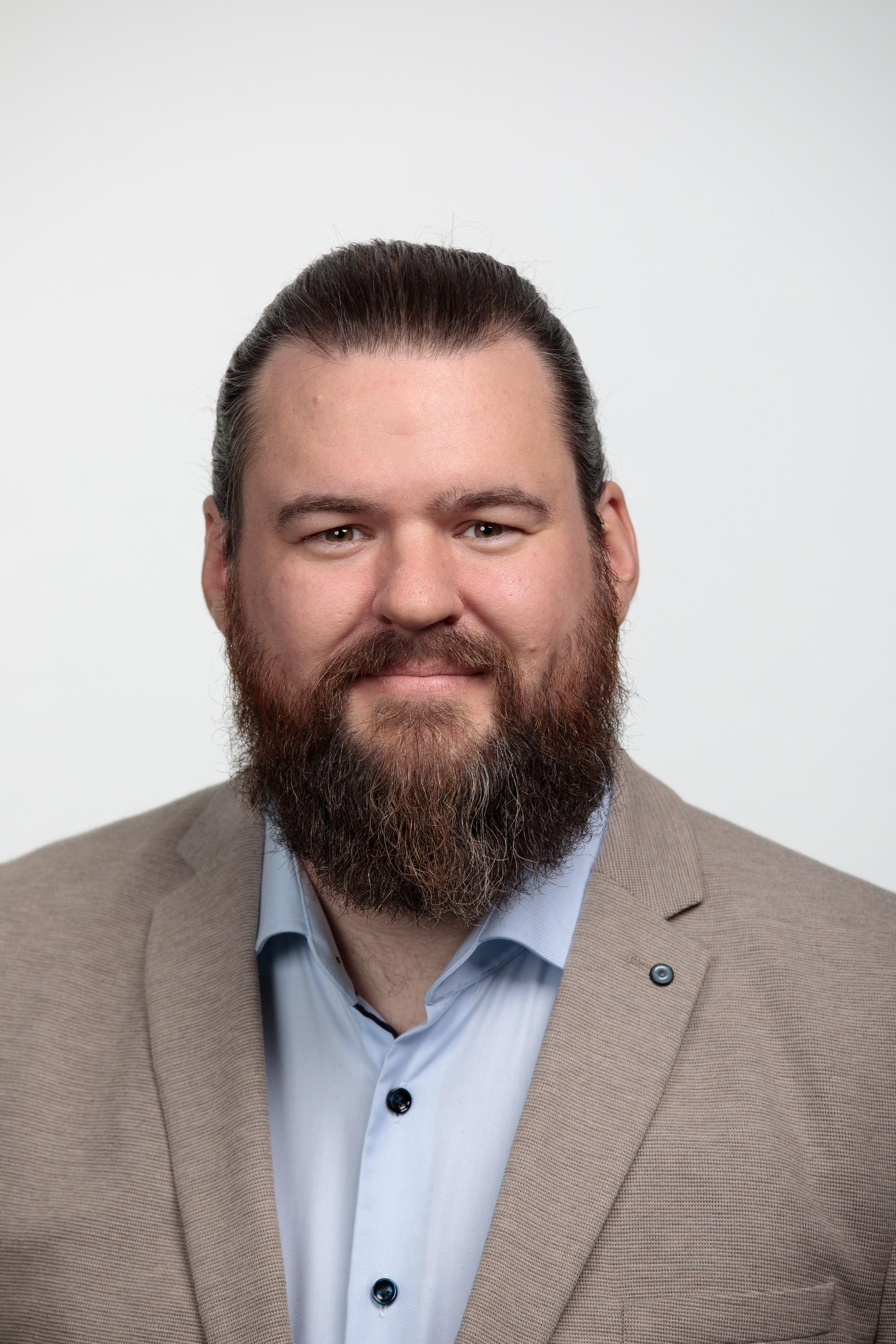 Portraitbild eines weissen Mannes mit braunen langen Haaren und Vollbart, er traegt ein helles Hemd und Jacket