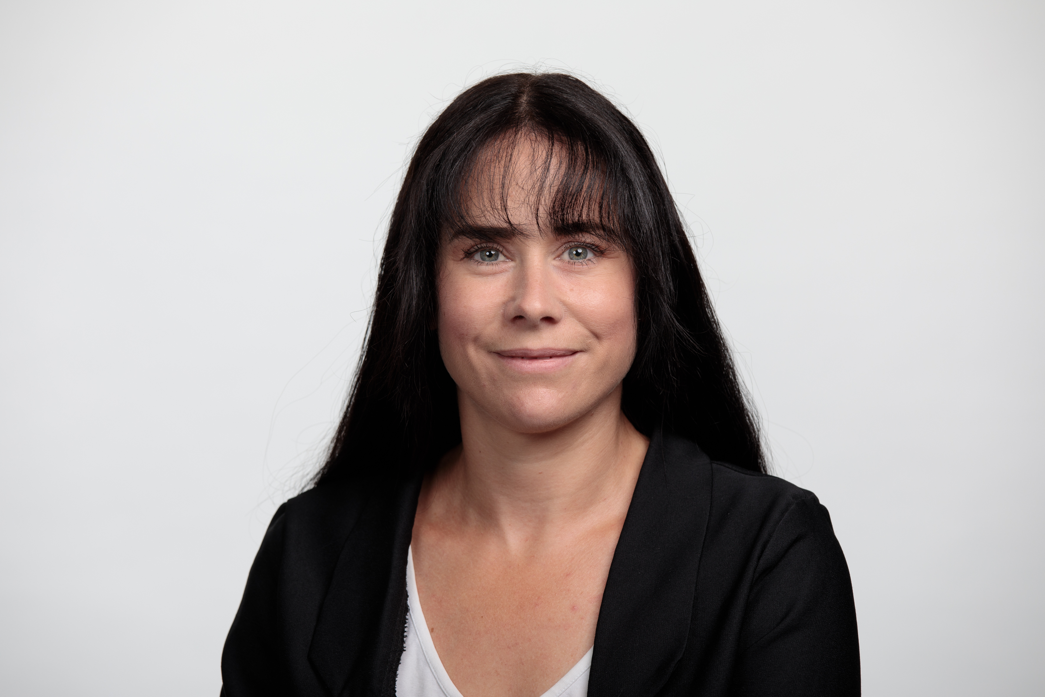 Portraitbild einer weissen Frau mit langen schwarzen Haaren, die einen schwarzen Blazer traegt