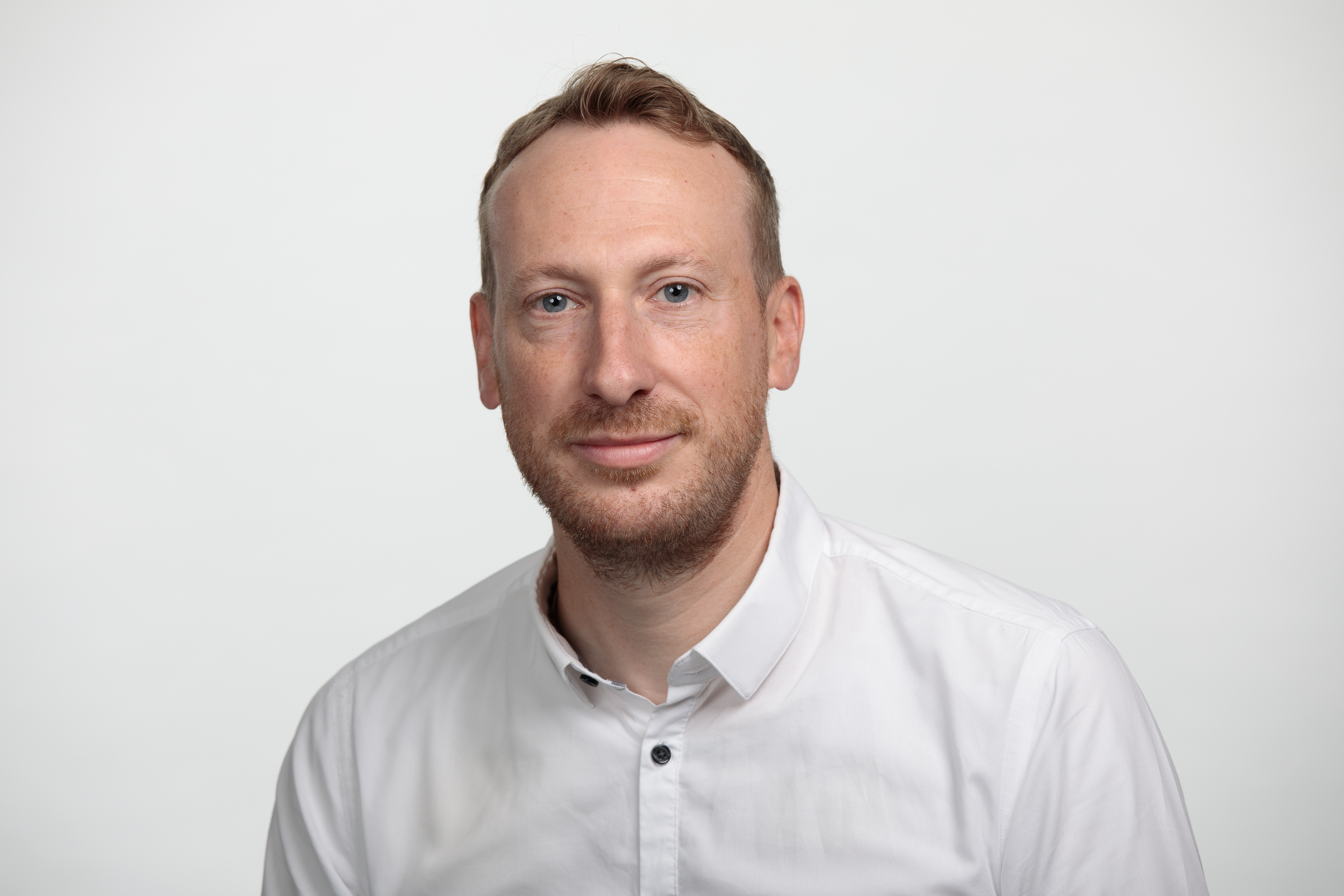 Portraitbild eines weissen Mannes mit kurzen blonden Haaren, der ein weisses Hemd traegt